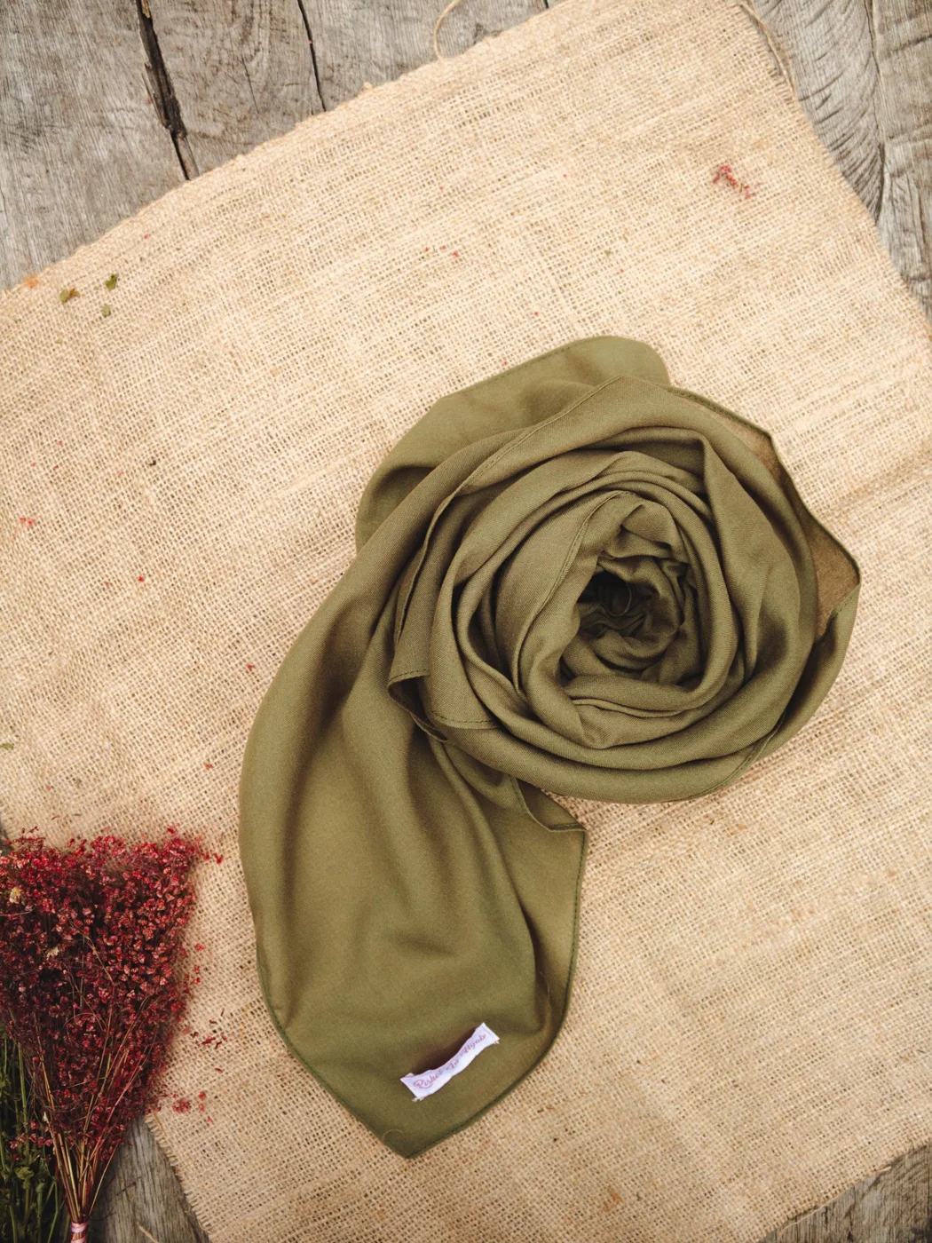 Smooth olive scarf loosely draped on a woven surface