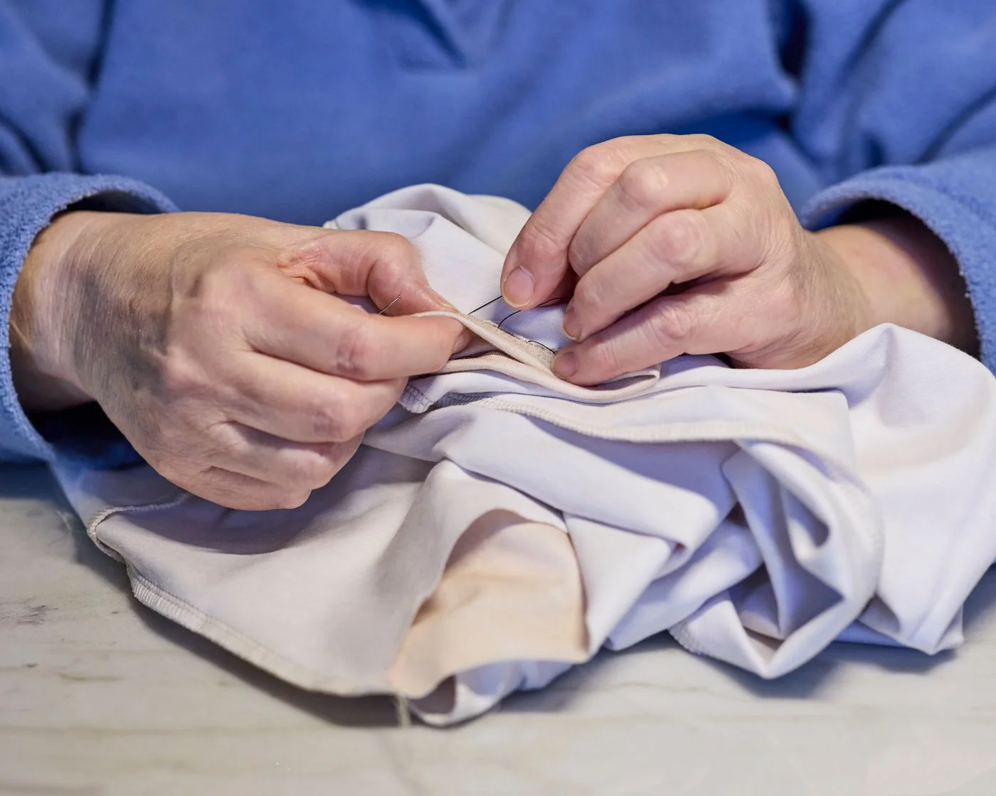 Hands repairing white fabric with needle and thread
