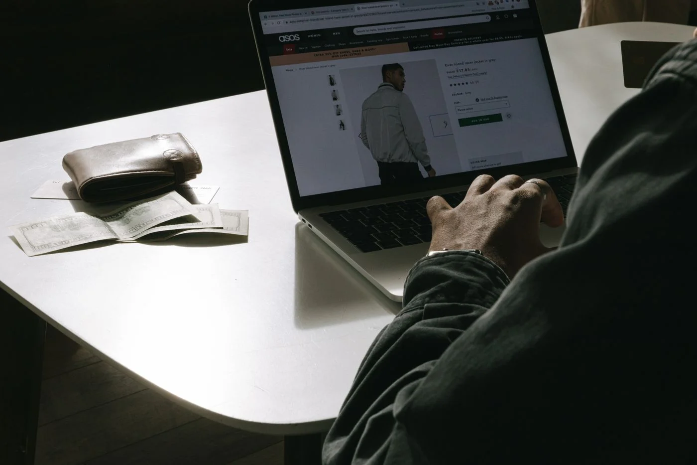 Shopper comparing clothing on a laptop with a wallet beside it